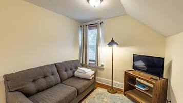 A cozy living room with a grey sofa, a standing lamp, a television on a wooden stand, and a patterned rug.