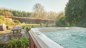 A hot tub surrounded by a wooden deck, a picnic table, and chairs.