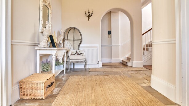 A hallway with a white console table, a mirror, a candelabra, a chair, and a wicker basket.