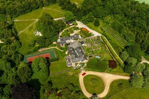 Vue aérienne d’une propriété comprenant une grande maison, un court de tennis et des jardins environnants.