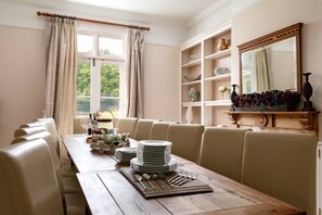 Ein Esszimmer mit einem langen Holztisch, gedeckt für mehrere Personen, umgeben von gepolsterten Stühlen.