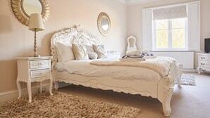 A bedroom with a large bed, two bedside tables, a dresser, a mirror, and a window with curtains.