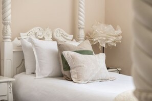 Una cama con ropa de cama blanca y varios almohadones, incluyendo uno a rayas verdes.
