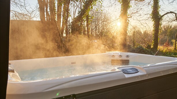 A hot tub with a control panel, surrounded by trees and a wooden deck. - Honeycomb Treehouse in the Heart of Dorset (Blandford Forum)
