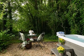 Een terras met een tafel, stoelen en een jacuzzi, omringd door groen.