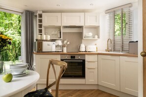 Een compacte keuken met witte kasten, een inbouwoven en een eethoek met een tafel voor twee personen.