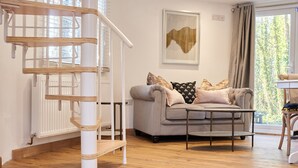 A modern living room with a grey sofa, a coffee table, and a wooden staircase. - Honeycomb Treehouse in the Heart of Dorset (Blandford Forum)