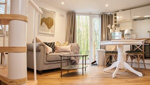 A modern living room with a sofa, a glass coffee table, and a dining area with a white table and chairs. - Honeycomb Treehouse in the Heart of Dorset (Blandford Forum)