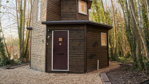 A small, wooden cabin with a dark brown door, a small window, and a chimney. - Honeycomb Treehouse in the Heart of Dorset (Blandford Forum)