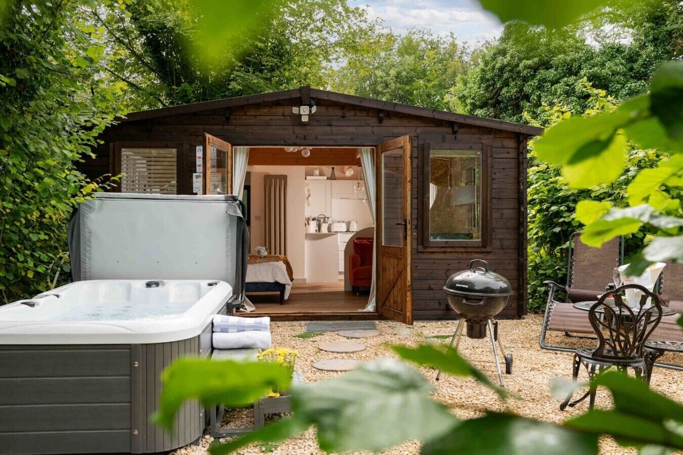Una cabaña de madera con la puerta abierta que muestra un dormitorio, un jacuzzi y una parrilla.