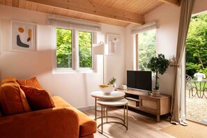 Een gezellige woonkamer met een bank, een televisie, een klein tafeltje met een schaal, en een raam met uitzicht op groen.