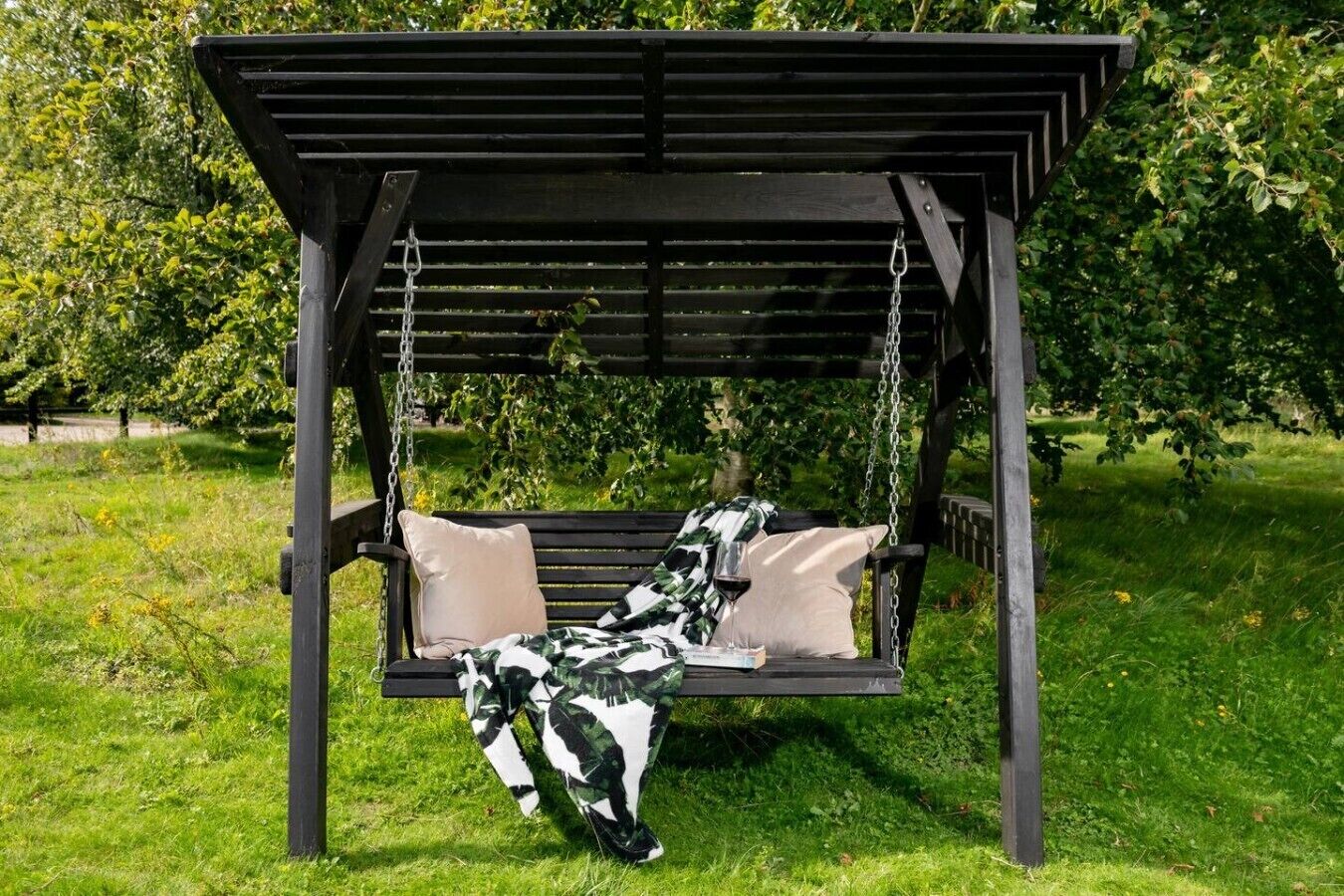 Ein Schaukelstuhl aus Holz mit Kissen, platziert in einem Garten mit Rasen und Bäumen.
