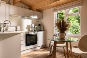 Een moderne keuken met witte kasten, een inbouwoven en een glazen tafel met een stoel.