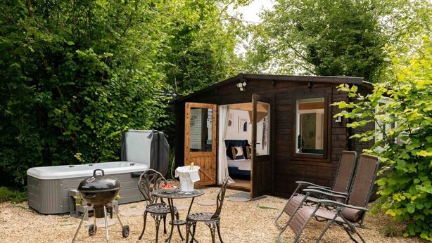Ein gemütlicher Außenbereich mit Whirlpool, Grill und einer Holzbeschreibung mit einer Tür zu einem Schlafzimmer.
