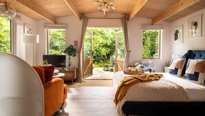 Ein Schlafzimmer mit Bett, einer Couch, einem Fernseher und einem Fenster mit Blick auf Grünflächen.