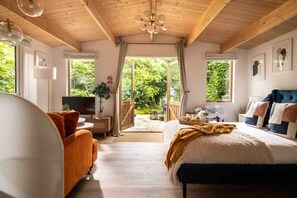 Een slaapkamer met een bed, een bank, een televisie en een raam met uitzicht op groen.