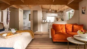 Een gezellig interieur met een bed, een oranje bank en een eethoek met een tafel.