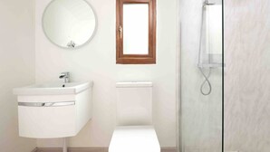 Ein Badezimmer mit einem weißen Waschbecken, einem runden Spiegel, einem Fenster mit Holzrahmen und einer Duschkabine aus Glas.