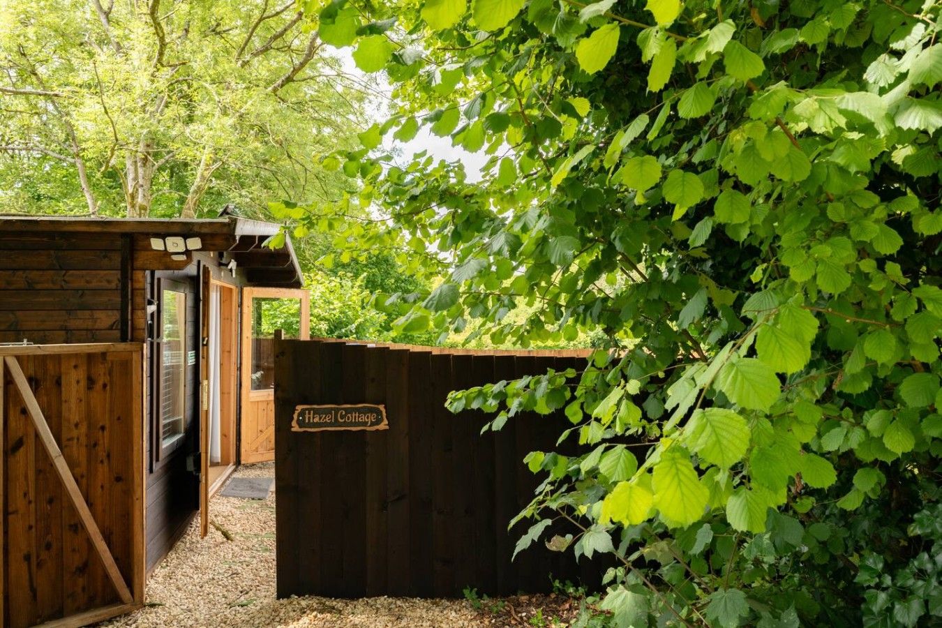 A wooden gate with a sign reading 'Hazel Cottage' leading to a wooden structure with a window.