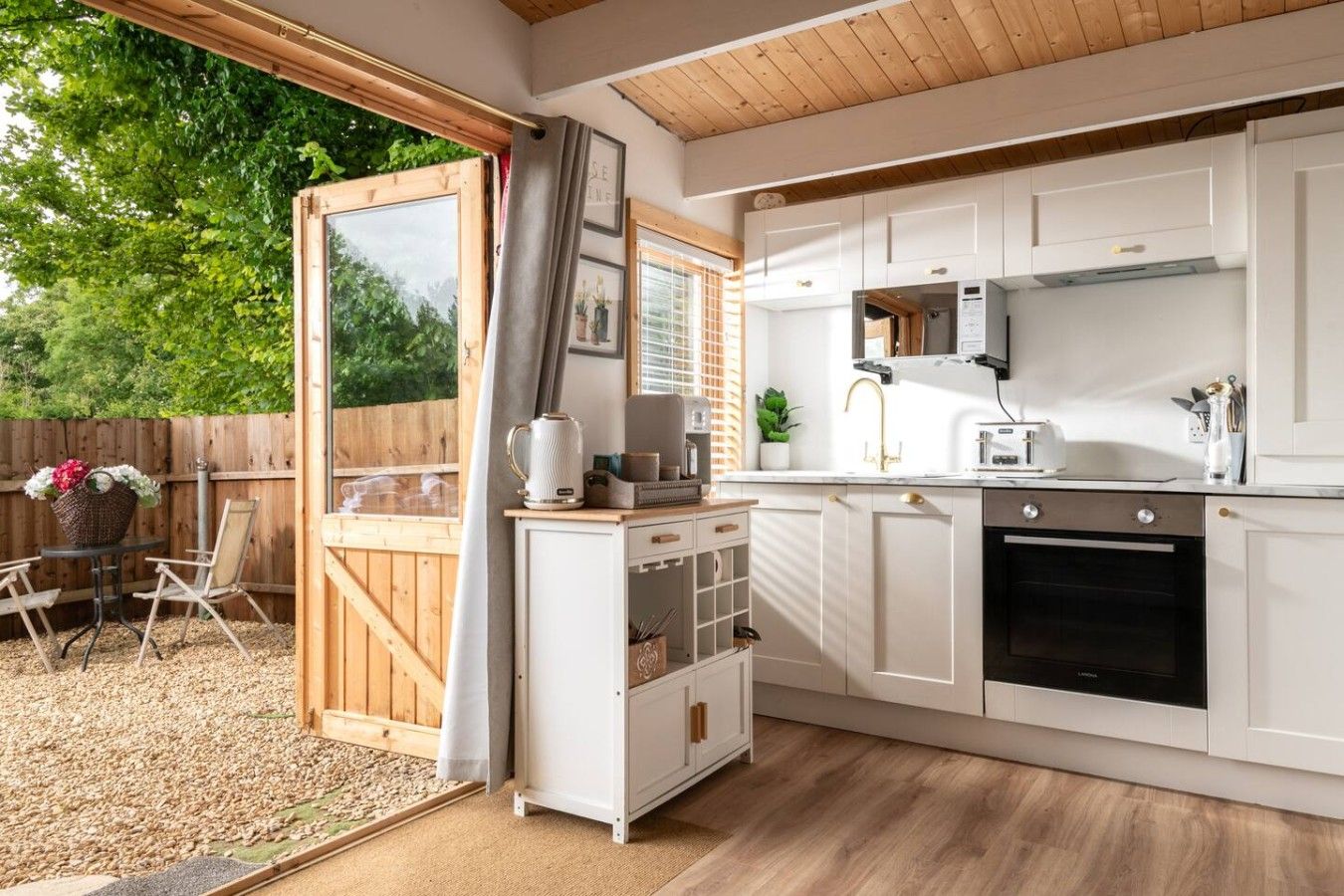 Een kleine keuken met witte kasten, een ingebouwde oven en een eethoek met een tafel en stoelen.