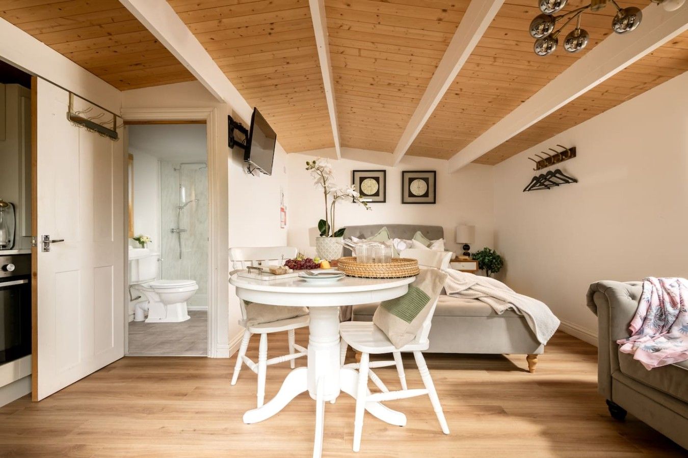 A cozy room with a wooden ceiling, a dining table with chairs, a bed, and a sofa.