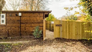 Une cabane en bois avec une porte en bois et une petite fenêtre. Il y a une pancarte sur la porte sur laquelle on peut lire « Hazel Cottage ».