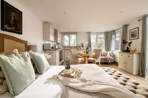 A spacious bedroom with a large bed, a dining area with a table and chairs, a kitchenette, and a view of the outdoors.