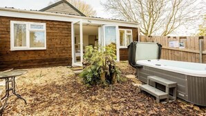 A wooden house with a hot tub, a patio table, and a leaf-covered ground.