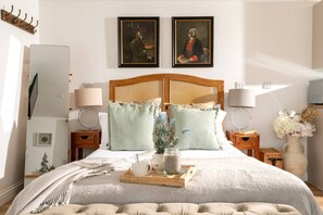 Quarto com uma cama grande, duas mesas de cabeceira, uma cabeceira de madeira e duas pinturas emolduradas acima da cama.