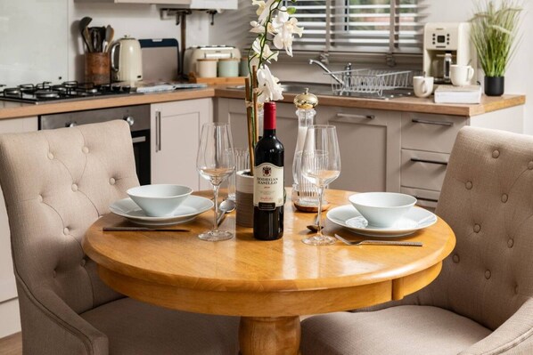 A dining table with two chairs, a bottle of wine, and several glasses.