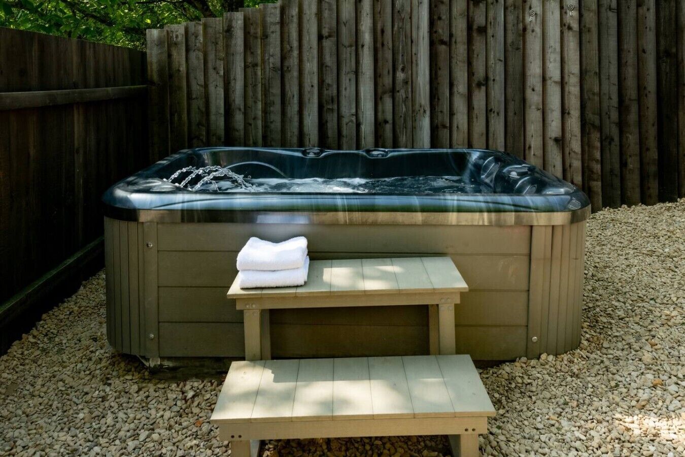 A hot tub with a wooden table and a bench in front, surrounded by gravel.