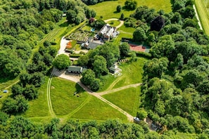 Ett flygbildsfoto av en fastighet med flera byggnader, en tennisbana och omgivande grönska.