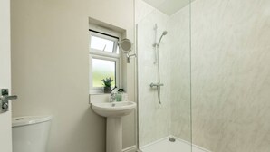 A bathroom with a toilet, a sink, a window, and a shower area.