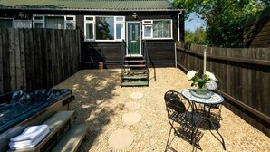 A wooden house with a gravel patio, a bench, a table with a vase of flowers, and a wooden fence.