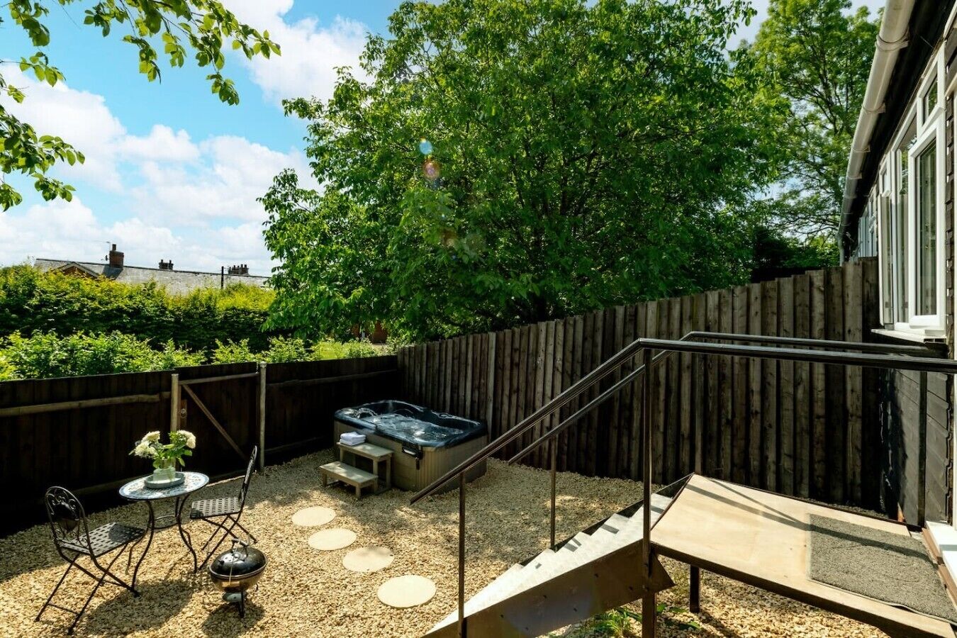 A backyard with a hot tub, a table with chairs, and a wooden fence.