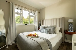 Un lit bien fait, avec des oreillers et un plateau contenant des aliments pour le petit-déjeuner, une table de chevet avec une lampe et une fenêtre avec des rideaux.