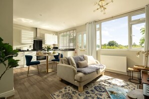 Une cuisine moderne avec des meubles blancs, un coin repas agrémenté d’une chaise bleue et une grande fenêtre donnant sur un paysage verdoyant.