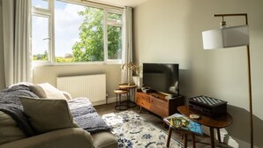 A living room with a sofa, a television, a small table with a magazine, and a lamp. - Dreamwood Woodland Retreat with Private Hot Tub (Blandford Forum)