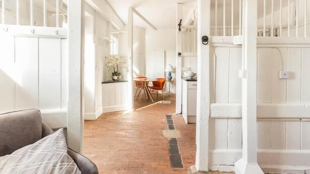 A bright, open-plan living space with a kitchen area, a dining table, and a sofa. - Historic Stable on a Private Vineyard (Blandford Forum)
