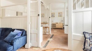 A room with a blue sofa, a wooden dining table, and a kitchen area in the background. - Historic Stable on a Private Vineyard (Blandford Forum)