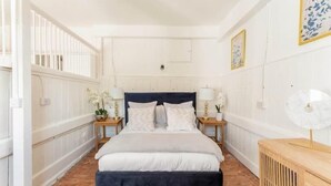 A bedroom with a large bed, white walls, a wooden floor, and two bedside tables with lamps. - Historic Stable on a Private Vineyard (Blandford Forum)