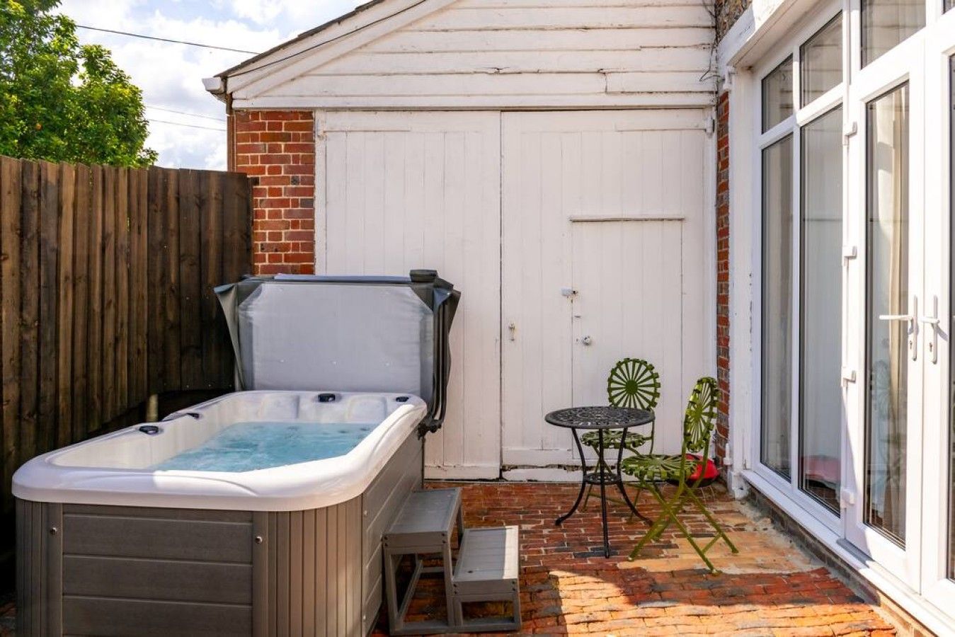 Un bain à remous situé dans un espace extérieur abrité, agrémenté d’une clôture en bois, d’une petite table et d’une chaise.