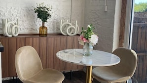 Ein Essbereich mit einem runden Tisch, zwei Stühlen, einer Blumenvase und einer strukturierten Wand.
