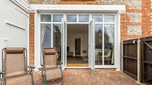 Eine Terrassenfläche mit zwei Metallstühlen, einem Ziegelboden und einer Glastür, die zu einem Innenbereich führt.