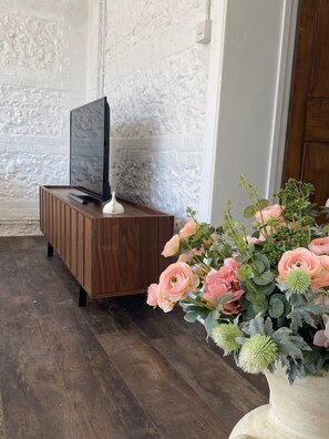Comfortable room with a flat-screen TV, a large vase with fresh flowers, and a dark wooden cabinet.