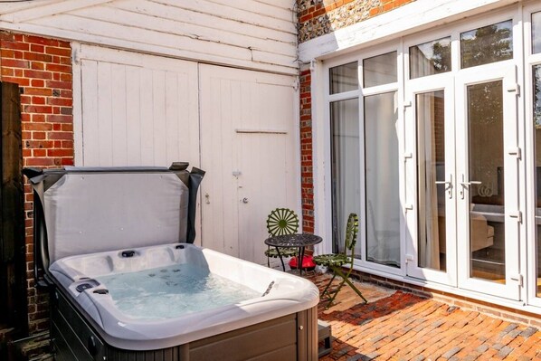 Un jacuzzi en un área exterior cubierta con una pared de ladrillo y una puerta corrediza de vidrio.