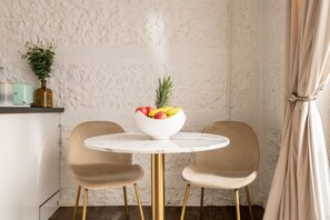 A dining area with a round marble table, two chairs, and a bowl of fruit.