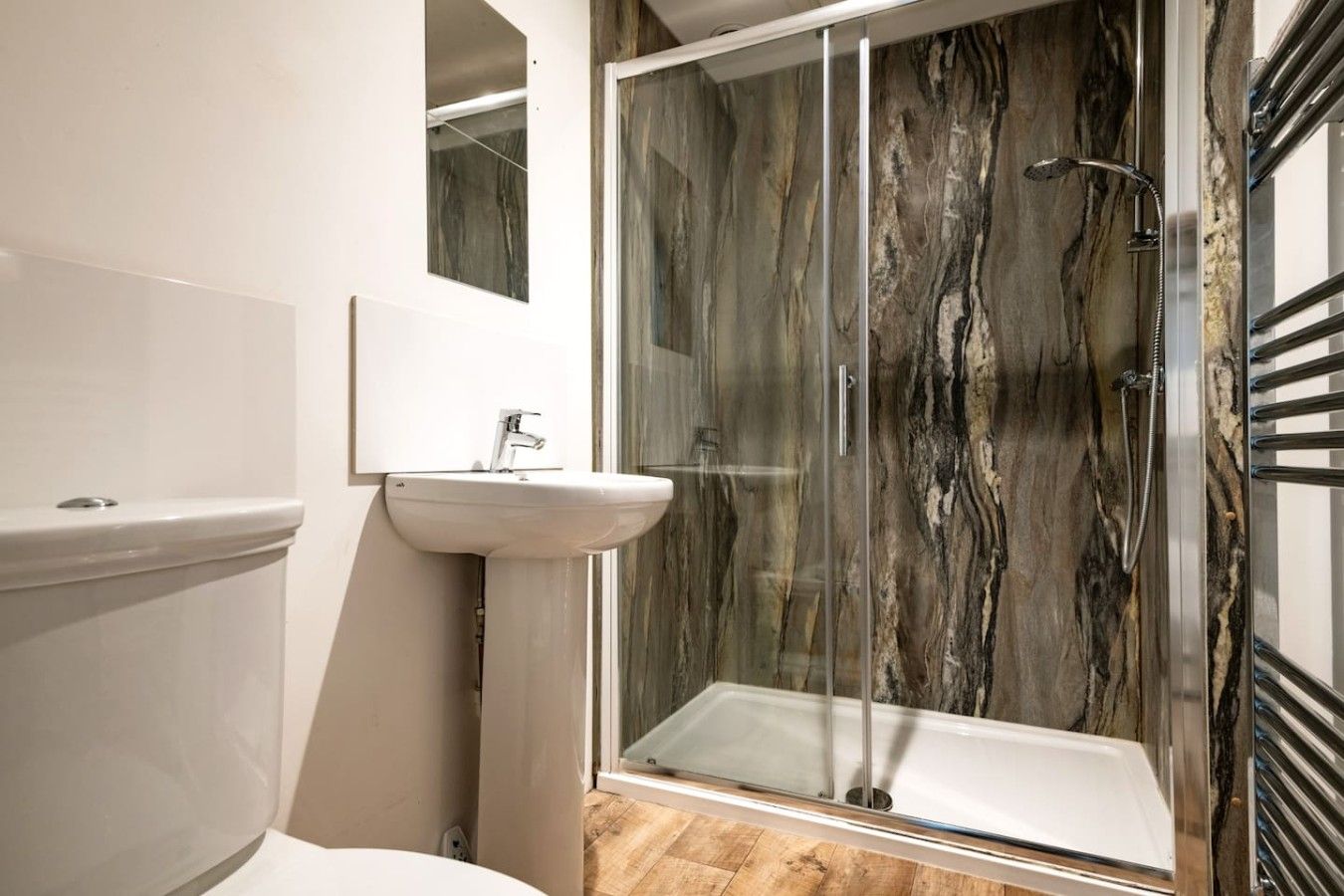 Une salle de bain moderne avec une douche à parois de verre, un lavabo blanc et un pare-baignoire en marbre.
