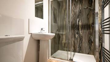 Une salle de bain moderne avec une douche à parois de verre, un lavabo blanc et un pare-baignoire en marbre.
