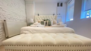 Ein Schlafzimmer mit geblattetem Bett, einem Heizkörper, einem Fenster mit Jalousien und einem Nachttisch mit Lampe und Dekoration.